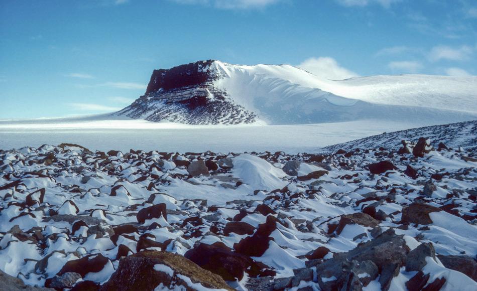 Die Siriusformation, in der sich marine Fossilien finden, ist in der Nähe von Mt. Fleming in der Antarktis exponiert. Das Muster im Schnee hinter den Felsen zeigt die vorherrschende Windrichtung über dem ostantarktischen Eisschild. Bild: Reed Scherer, 1986, Northern Illinois University