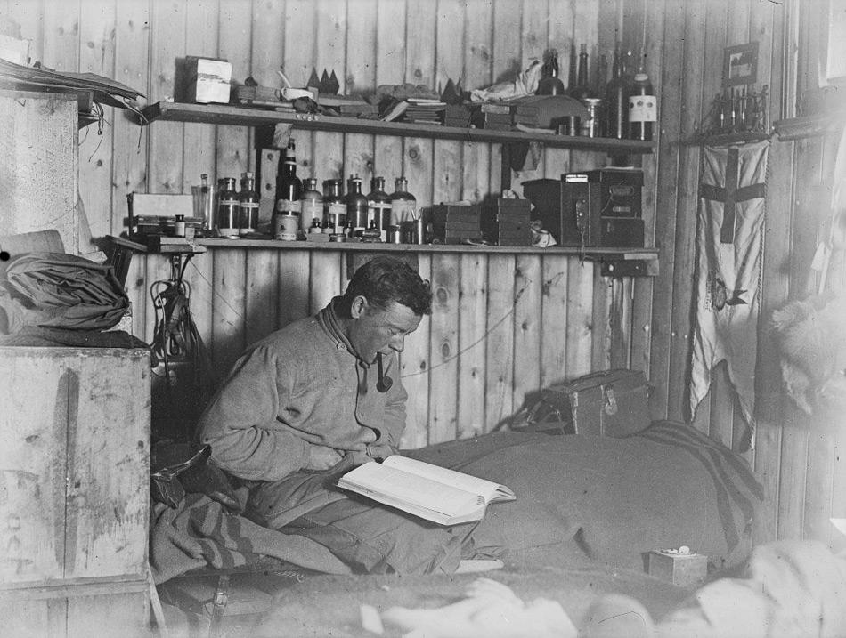 George Murray Levick beim Pfeifenrauchen und Lesen auf seinem Bett in der Hütte von Kap Adare. © P48/14/5 Scott Polar Research Institute, Universität Cambridge