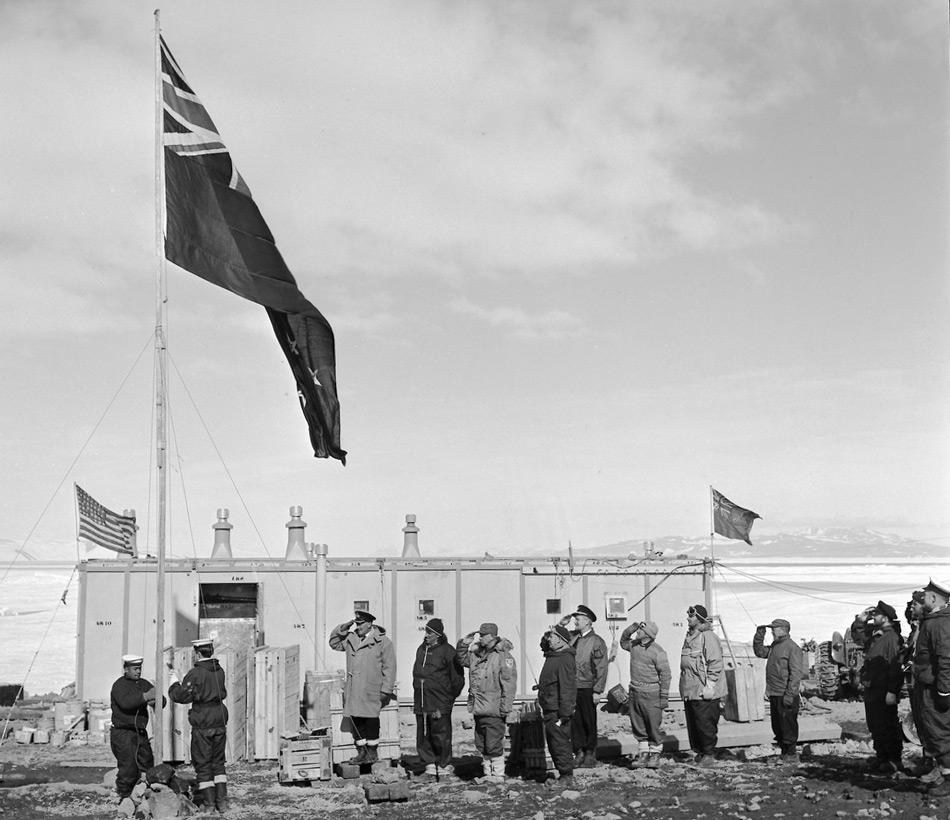 Hissen der neuseeländischen Flagge an Scott Base am 20. Januar 1957 vor der TAE-Hütte. Zeugen sind Mitglieder der neuseeländischen und amerikanischen Antarktis-Expeditionen. (Foto: John Claydon)